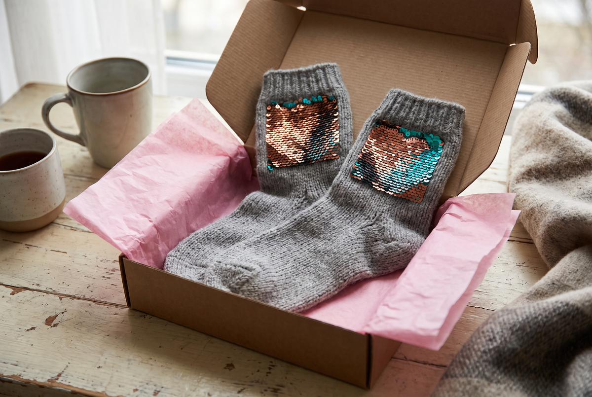 Paire de chaussettes à paillettes réversibles posée dans une boîte cadeau ouverte avec du papier de soie